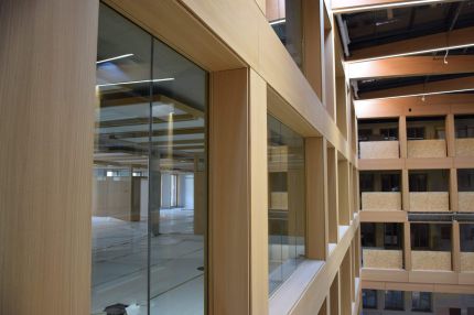 Seitlicher Blick entlang der holzfurnierten Glasfassade im Atrium – IHK Nürnberg