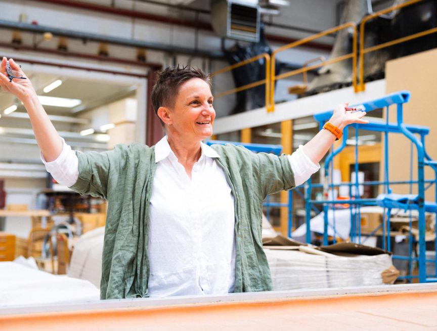 Eine Frau erklärt begeistert Raumakustik in einem Arbeitsraum voller Materialien. | © Staudigel