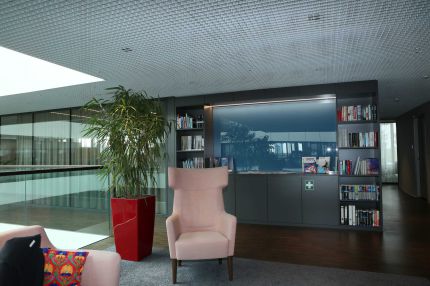 Leseecke mit Ohrensessel, Regalwand und Rasterdecke an der Galerie – AEB-Zentrale, Stuttgart