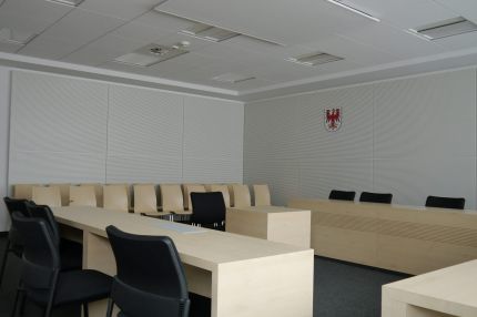Sitzungssaal mit weißen Schlitzplatten an den Wänden, Blick zur Richterbank – Sparkasse Spree-Neiße, Cottbus