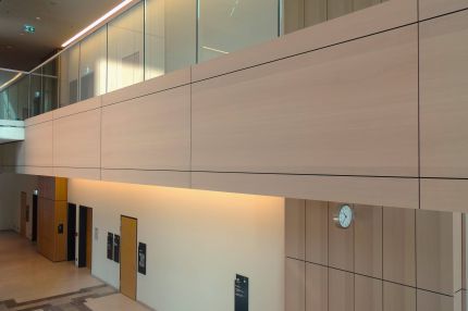 Galeriebrüstung mit großformatiger Holzverkleidung über der Halle mit Wanduhr – Justizzentrum Bochum