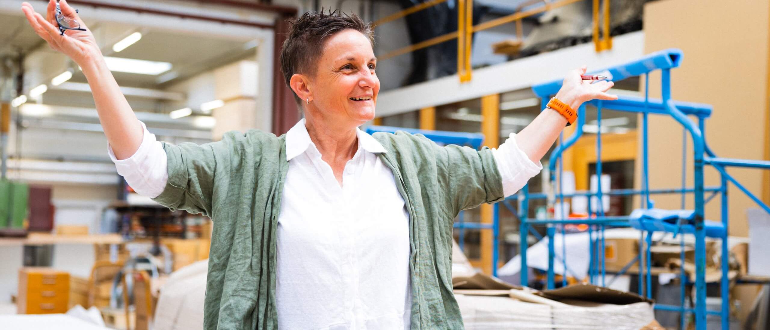 Eine Frau erklärt begeistert Raumakustik in einem Arbeitsraum voller Materialien. | © Staudigel