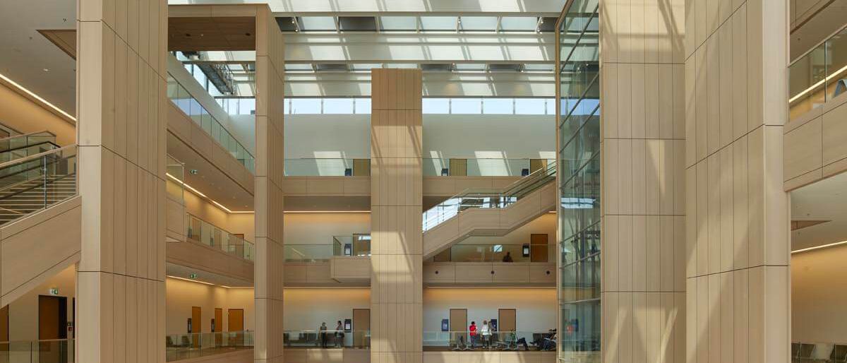 Lichthof unter Glasdach mit holzverkleideten Pfeilern und Galerien – Justizzentrum Bochum