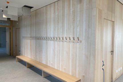Flur mit Holz-Wandverkleidung, Garderobenhaken, Sitzbank und Akustikdecke – Bildungskampus Köln