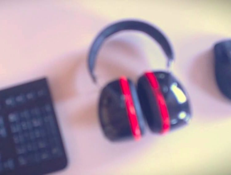 Ein unscharfes Bild von einer Tastatur, Maus und Staudigel Gehörschutz auf einem Tisch.