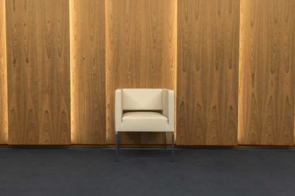 Weißer Sessel mittig vor hinterleuchteter Holzfurnier-Wand, Teppich und Steinboden – Deutsche Rentenversicherung, Würzburg