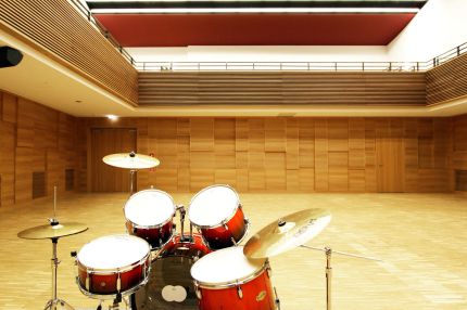 Saal mit Schlagzeug, Holz-Wandverkleidung und Galerie mit Lamellenbrüstung – Musikschule Essenbach
