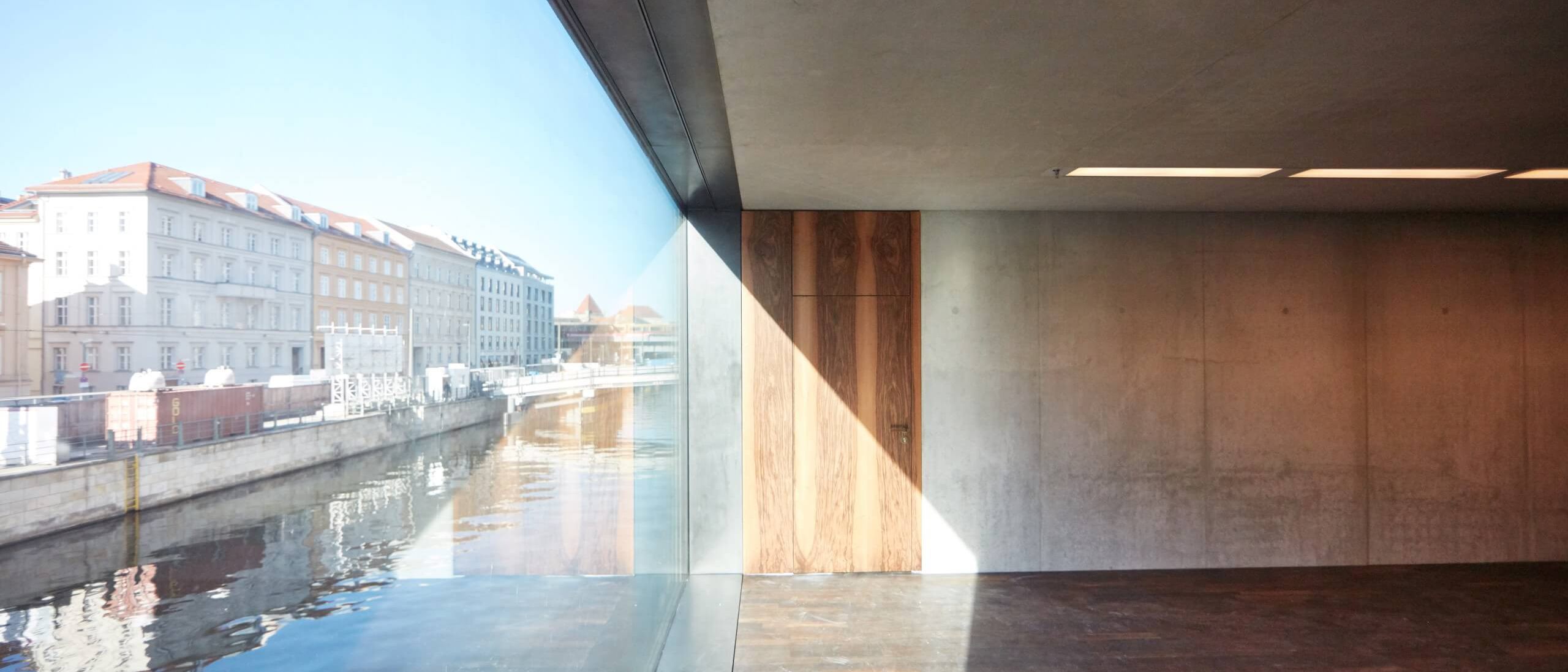 Raum an der Glasfassade mit Blick auf den Kupfergraben, Sichtbeton und Nussbaumtür – James-Simon-Galerie, Berlin
