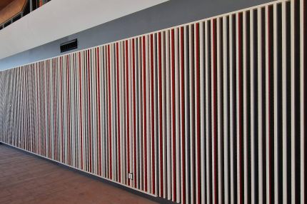 Lange Wand mit weißen Holzlamellen vor roten und grauen Akustikfeldern – Mensa Würzburg