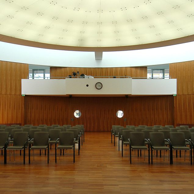 Saal mit Stuhlreihen, Holz-Wandverkleidung, Empore und ovaler Lichtdecke – IHK Potsdam
