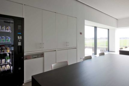 Pausenraum mit geschlossener Schrankwand, Lochplattendecke und Blick ins Freie – Willy Naessens Group, Belgien