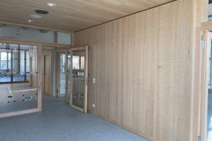 Flur mit gelochter Holz-Wandverkleidung, Holzdecke und Glastüren – Bildungskampus Köln