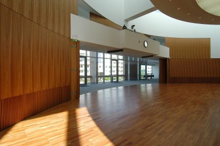 Zum Foyer geöffneter Saal mit gebogener Holzwand und Sonnenlicht auf dem Parkett – IHK Potsdam
