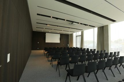 Konferenzsaal mit Stuhlreihen, Leinwand und dunkler Holzfurnier-Wandverkleidung – AEB-Zentrale, Stuttgart