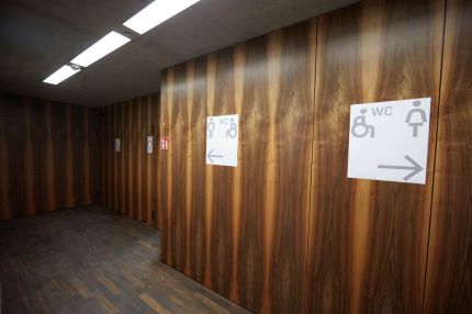 Vorraum der Toiletten mit Wandverkleidung in Nussbaum-Furnier und Beschilderung – James-Simon-Galerie, Berlin