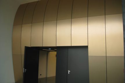 Bronzefarbene, gebogene Wandplatten über offener Doppeltür zum Saal – Bürgerhaus Lechner Bräu
