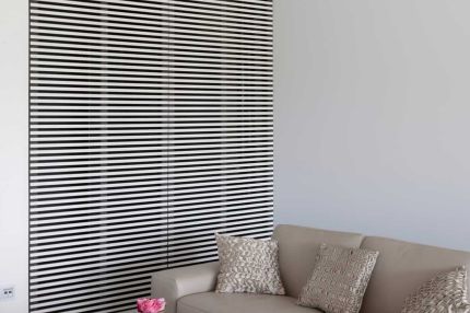 Sitzecke mit Sofa vor einem Wandelement mit schwarz-weißen Lamellen – Willy Naessens Group, Belgien