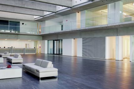 Atrium mit weißen Sofas, Galerie mit Glasbrüstung und Lamellenwand – Willy Naessens Group, Belgien