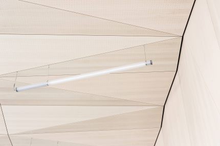 Detail der facettierten Lochplatten-Decke mit Stableuchte am Wandanschluss – Gymnasium Oberursel