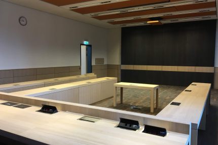 Sitzungssaal mit dunkler Holzwandverkleidung, hellem Querband und Akustikdecke – Justizzentrum Bochum