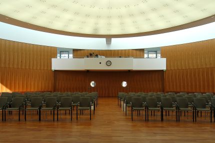 Saal mit Stuhlreihen, Holz-Wandverkleidung, Empore und ovaler Lichtdecke – IHK Potsdam