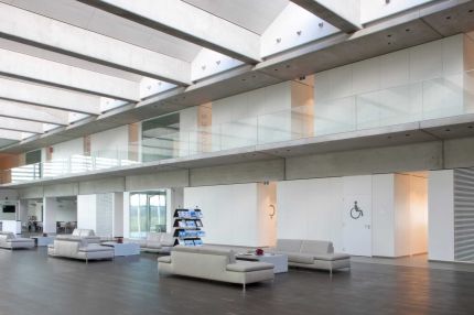Weites Atrium mit Lounge-Möbeln, Glasbrüstung der Galerie und Lamellenwand – Willy Naessens Group, Belgien