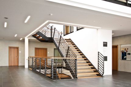 Treppenhalle mit Stahl-Holz-Treppe und Lochplattendecke mit Lichtfugen – Musikschule Essenbach