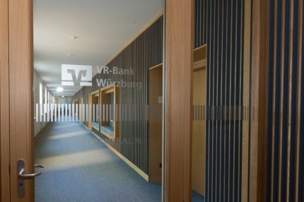 Blick durch Glastür mit VR-Bank-Logo in den Flur mit Lamellenwand – MOZ-Areal VR-Bank, Würzburg