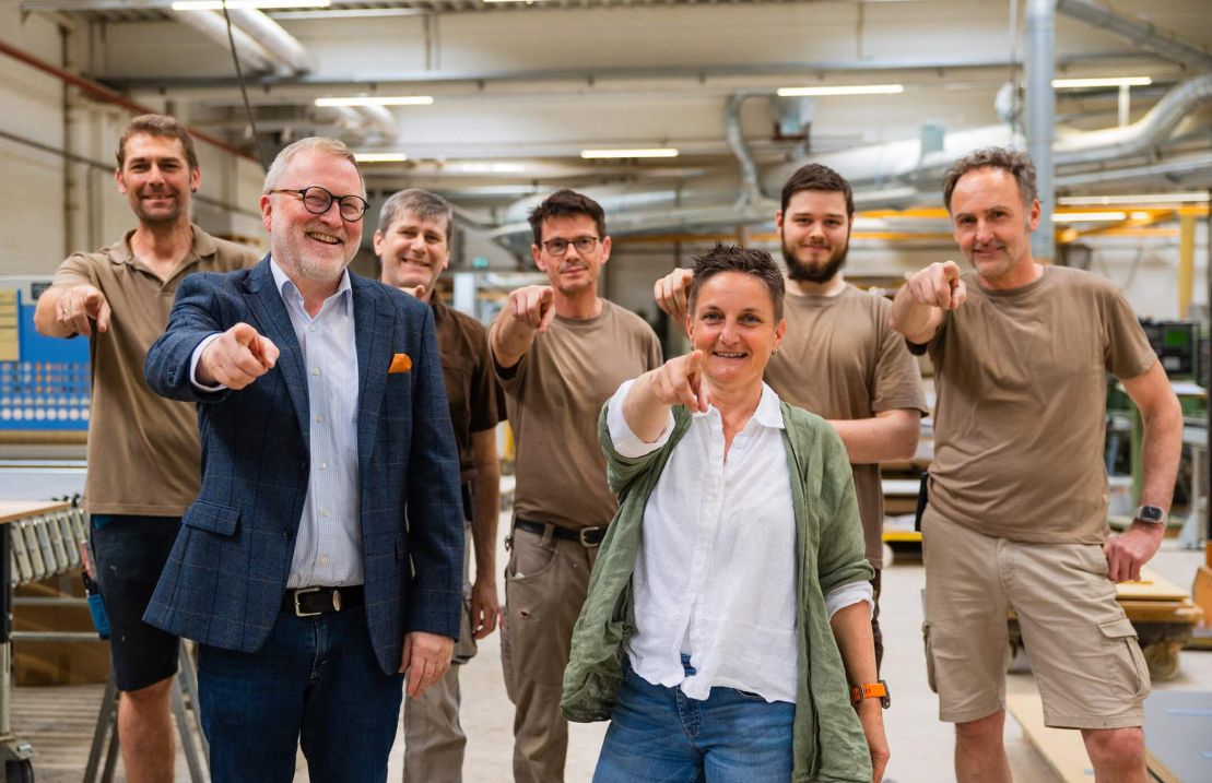 Eine Gruppe von Fachleuten lächelt und zeigt auf die Kamera in einem Workshop für akustische Lösungen und Wandverkleidungen.