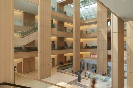Blick von der Treppe in den Lichthof mit holzverkleideten Pfeilern und Lochdecke – Justizzentrum Bochum