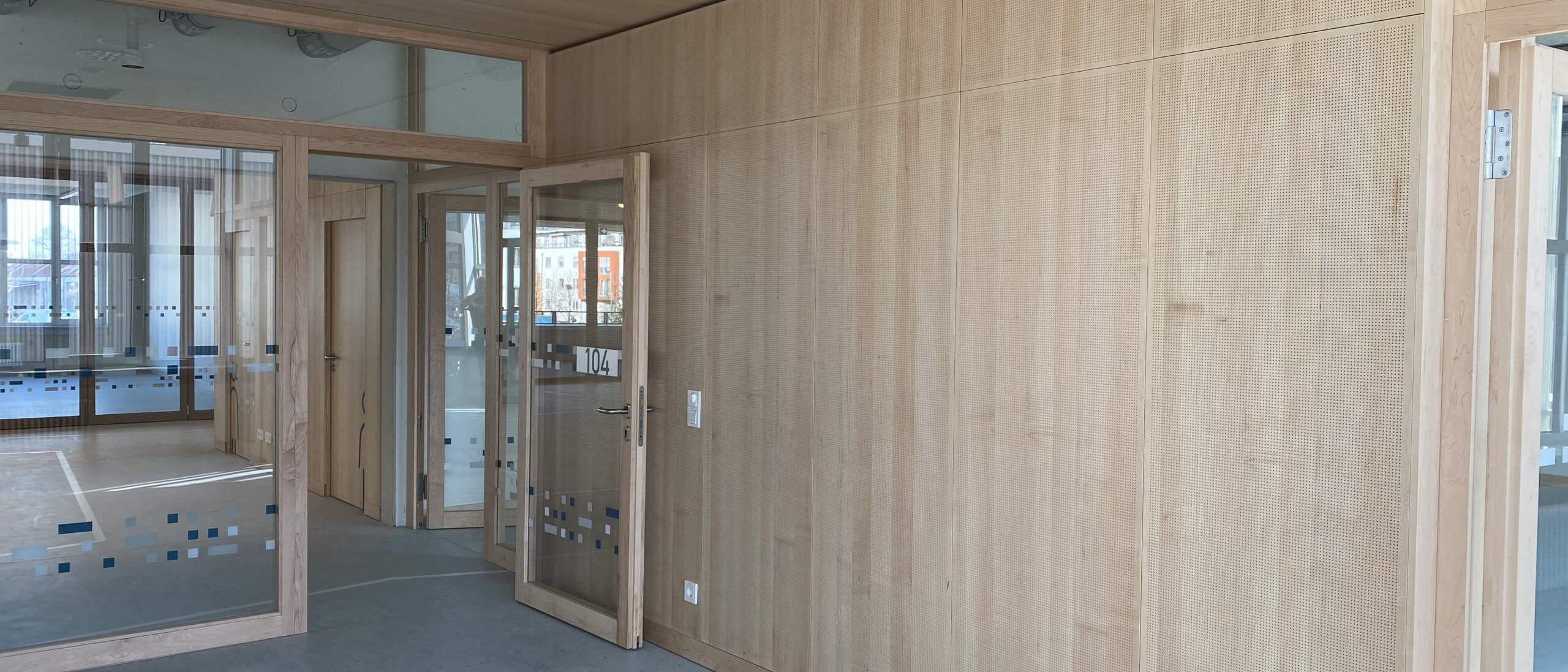 Flur mit gelochter Holz-Wandverkleidung, Holzdecke und Glastüren – Bildungskampus Köln