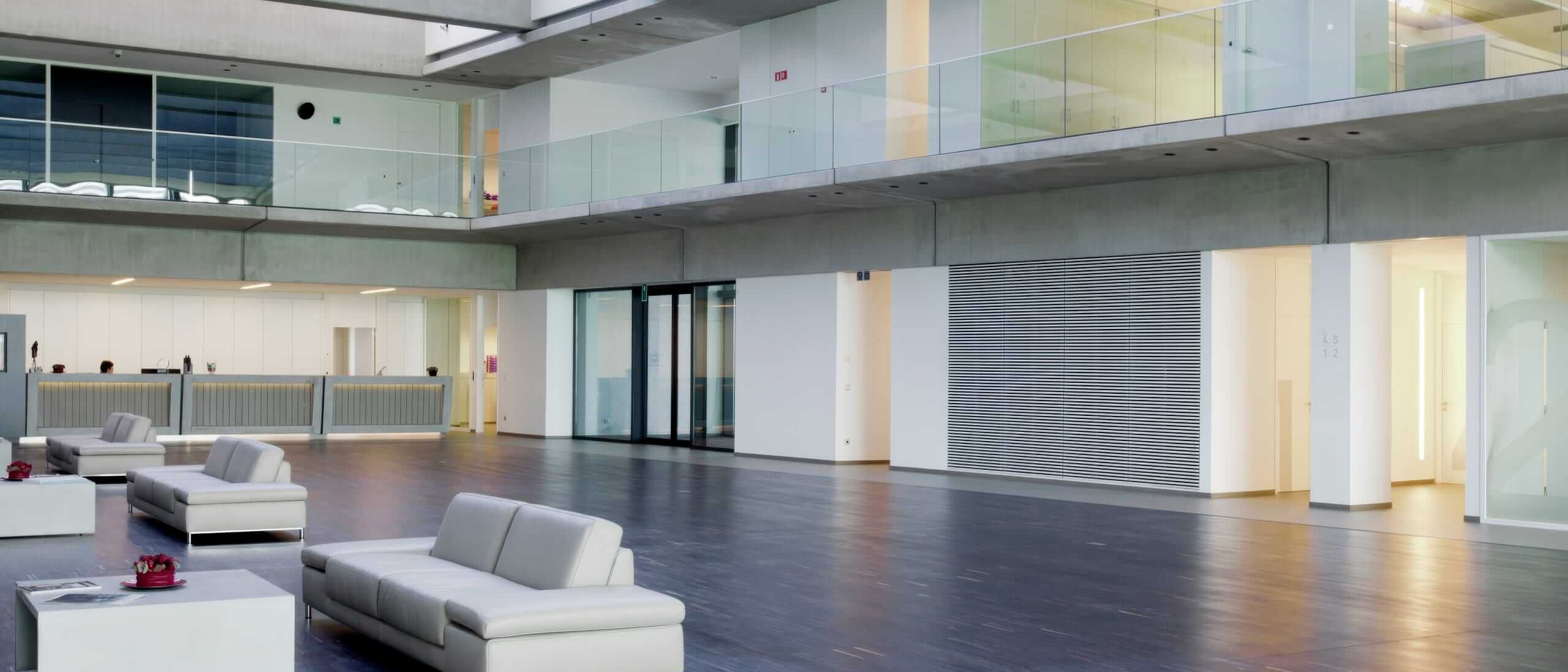 Atrium mit weißen Sofas, Galerie mit Glasbrüstung und Lamellenwand – Willy Naessens Group, Belgien