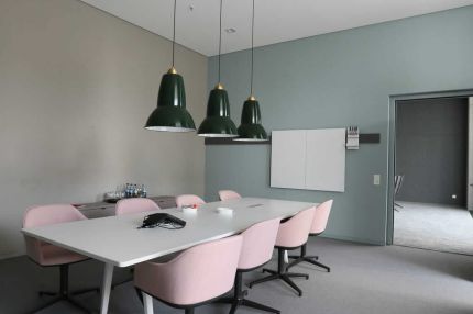 Besprechungsraum mit rosa Stühlen, grünen Pendelleuchten und Whiteboard – AEB-Zentrale, Stuttgart