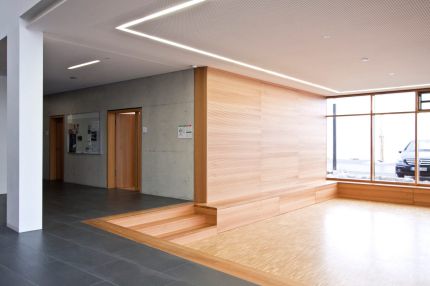 Foyer mit Holz-Wandverkleidung, Sitzstufen und Lochplattendecke mit Lichtband – Musikschule Essenbach