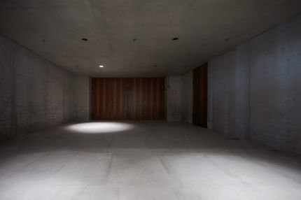 Sichtbetonraum mit Flügeltüren in Nussbaum-Furnier und Lichtkegel am Boden – James-Simon-Galerie, Berlin
