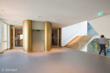 Foyer mit goldfarbenen Rundsäulen am Aufzug und Treppe mit Wandbild – MOZ-Areal VR-Bank, Würzburg