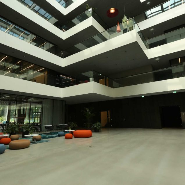 Lichthof mit farbigen Sitzpoufs und dunkler Holzwandverkleidung im Erdgeschoss – AEB-Zentrale, Stuttgart