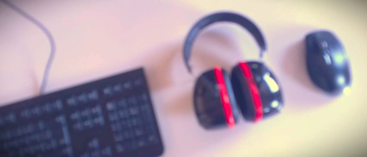 Ein unscharfes Bild von einer Tastatur, Maus und Staudigel Gehörschutz auf einem Tisch.