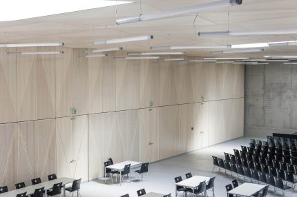 Saal mit heller Holz-Wandverkleidung, integrierten Türen und Sichtbetonwand – Gymnasium Oberursel
