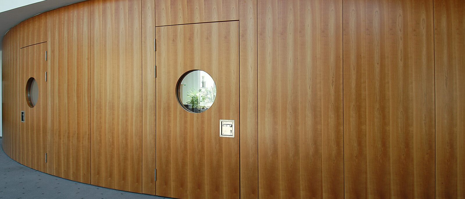 Gebogene Holz-Wandverkleidung mit Türen und Bullaugenfenstern, Außenseite – IHK Potsdam