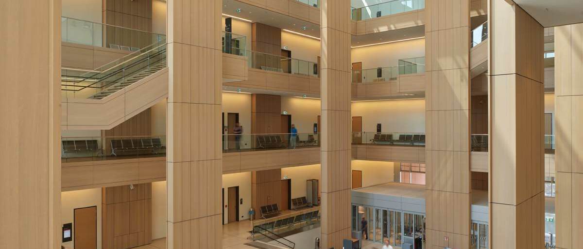 Blick von der Treppe in den Lichthof mit holzverkleideten Pfeilern und Lochdecke – Justizzentrum Bochum