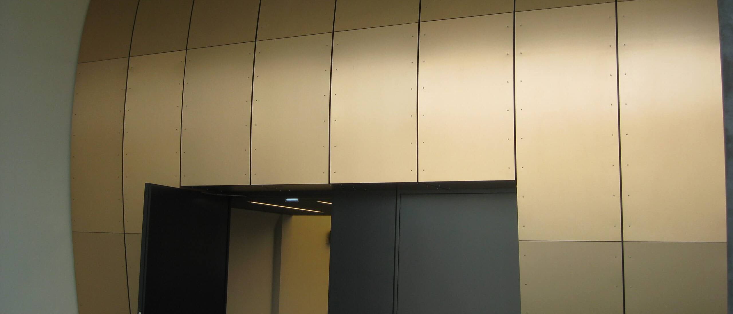 Bronzefarbene, gebogene Wandplatten über offener Doppeltür zum Saal – Bürgerhaus Lechner Bräu