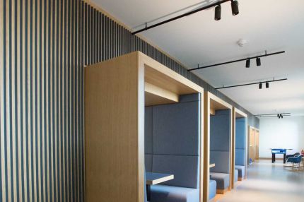 Aufenthaltsbereich mit Sitzkabinen aus Eiche vor Lamellenwand und Strahlern – MOZ-Areal VR-Bank, Würzburg