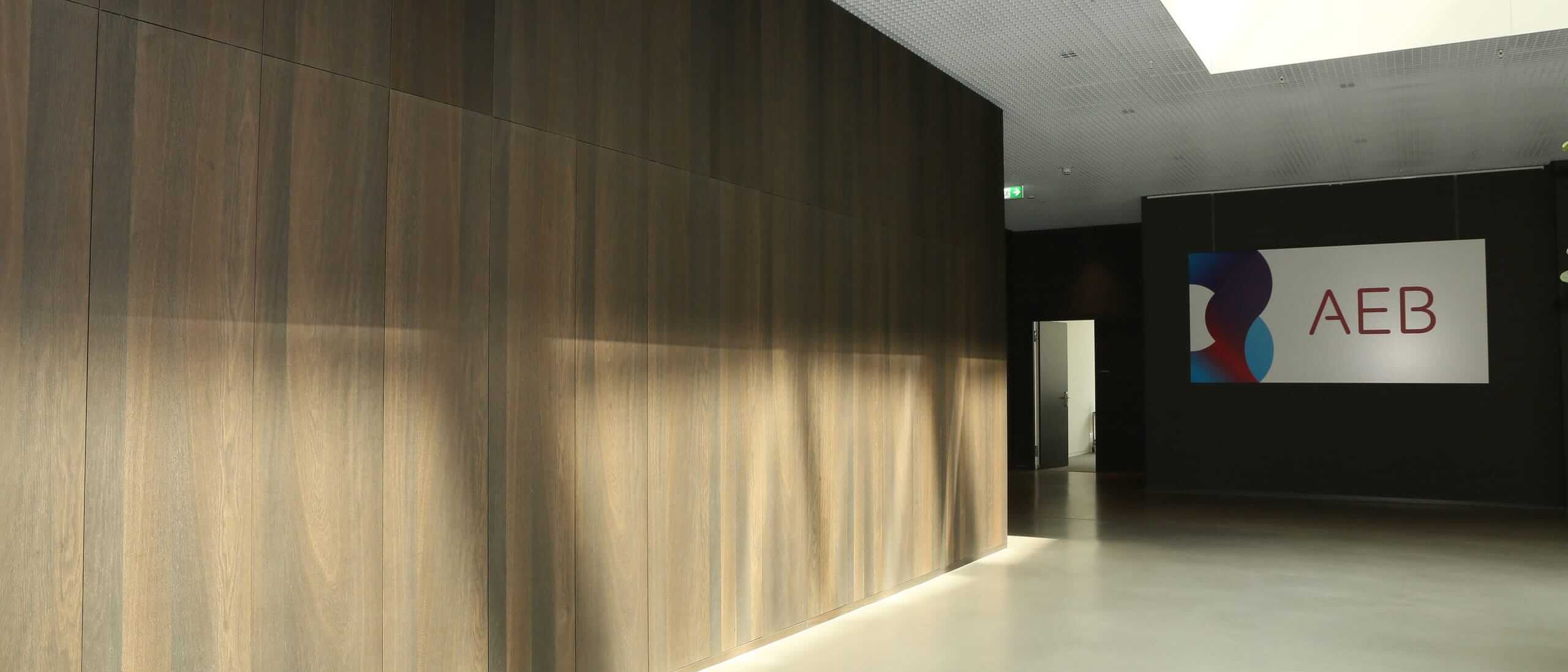 Foyer mit Wandverkleidung in dunklem Holzfurnier, Streiflicht und Firmenlogo – AEB-Zentrale, Stuttgart