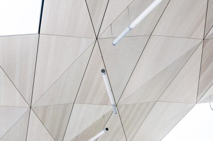 Facettierte Decke aus dreieckigen Lochplatten mit abgehängten Stableuchten – Gymnasium Oberursel