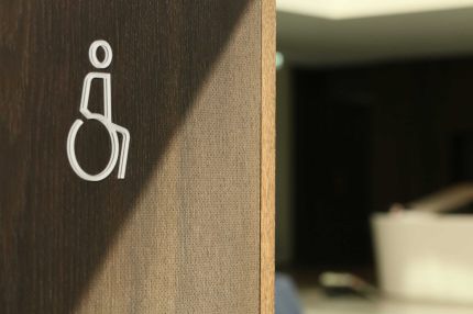 Detail Rollstuhl-Piktogramm auf mikroperforierter Wandverkleidung in dunklem Furnier – AEB-Zentrale, Stuttgart