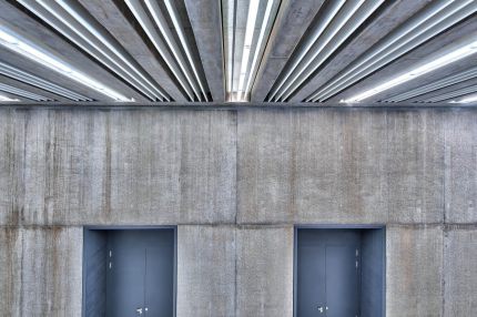 Lamellendecke mit Lichtbändern über Betonwand mit zwei Türnischen – Gymnasium Oberursel