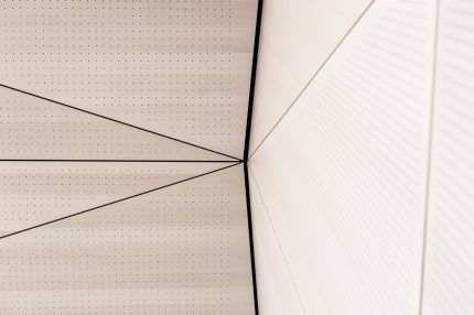 Detail des Eckpunkts zwischen Lochplatten-Decke und facettierter Wandverkleidung – Gymnasium Oberursel