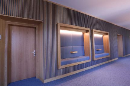 Zwei gepolsterte Sitznischen mit Lichtband in der Lamellenwand neben Eichentür – MOZ-Areal VR-Bank, Würzburg