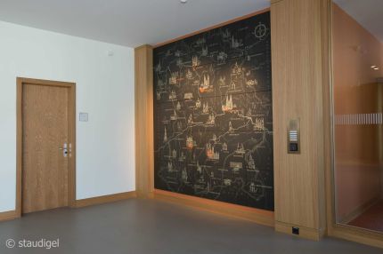 Foyer mit dunklem Landkarten-Wandbild zwischen Eichenpfeilern und Eichentür – MOZ-Areal VR-Bank, Würzburg